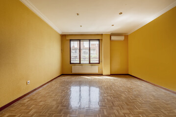 An empty front windowed living room with a long aluminum radiator below