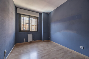 An empty living room with a blue wall, cheap wooden floors and oak doors and a bay window with steel bars
