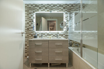 A bathroom with a glass-enclosed shower, colored tiles, a wooden chest of drawers