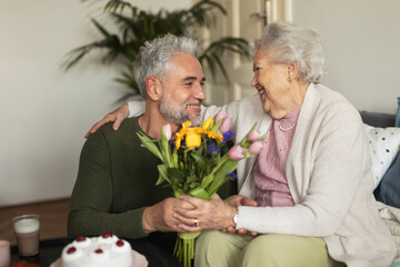 Mature man celebrating with his senior mother at her apartment.