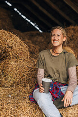 Naklejka na ściany i meble A beautiful smiling blond woman sitting on a haystack.