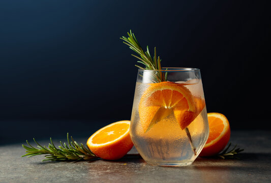Cocktail gin tonic with ice, rosemary, and orange on a stone table.