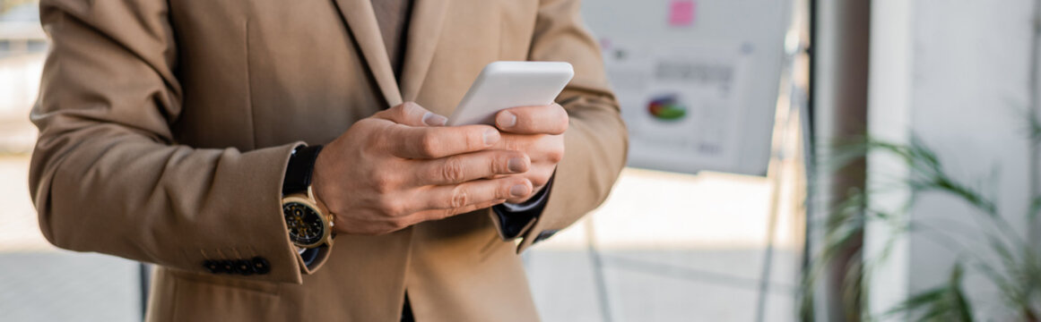 cropped view of accomplished entrepreneur wearing beige blazer and stylish wristwatch, using mobile phone near flip chart with business analytics on blurred background, banner