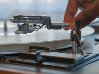 Fototapeta premium Detail of a female hand placing the needle on the track of a white vinyl record. Vintage turntable