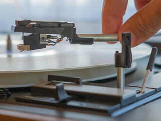 Detail of a male hand placing the needle on the track of a white vinyl record. Vintage turntable