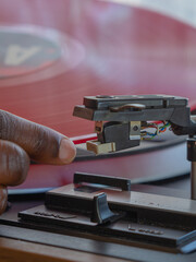 Detail of a female hand placing a red vinyl record on a vintage turntable