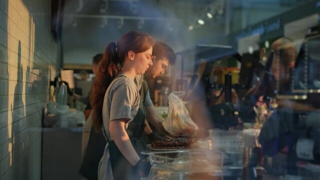 Cashiers In Uniform Serving Customers At The Checkout In A Grocery Store. Small Business Concept