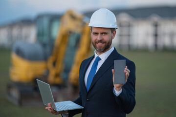 Architect at a construction site. Architect man in helmet and suit at modern home building construction. Architect with a safety vest and suit. Confident architect standing at house background.