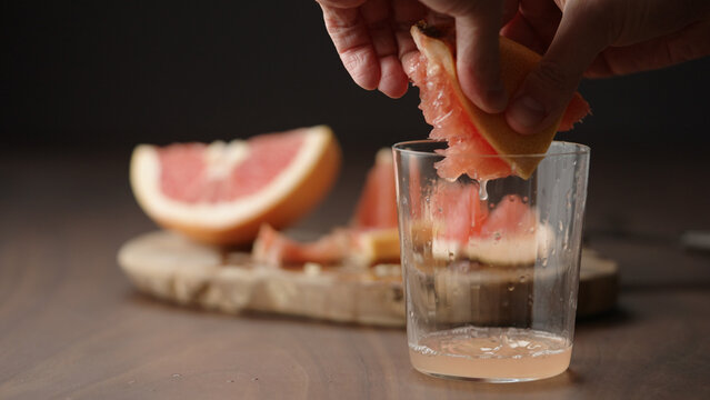 man squeeze grapefruit into tumbler glass on wood table
