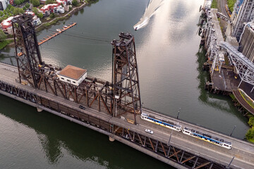 Light rail train crosses over a bridge while a boat comes up the river