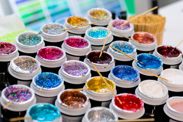Samples of cosmetic makeup glitter with wooden stick in row on counter for sale in cosmetics shop, tradeshow - close up. Glamour, fashion, make up, beauty and skincare concept