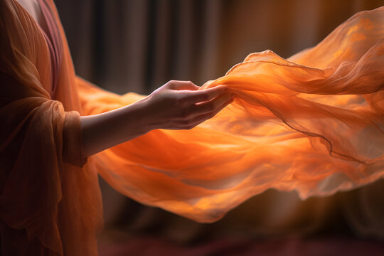 A soft flowing shawl is thrown over a woman's hand. Orange colors. 