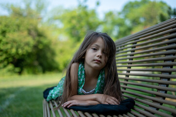 cute preschool girl smiling for portrait while laying on park bench