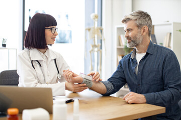 Beautiful short-haired doctor in glasses removing tonometer from wrist before entering patient's...