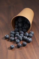 Ripe blueberries spilling from paper cup on wood table