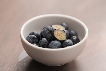 Fresh blueberries in white bowl one berry is cut in halves