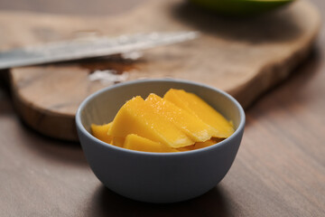 Naklejka na ściany i meble Fresh sliced mango in a ceramic bowl on walnut table