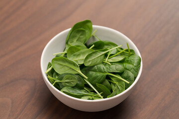 Fresh spinach leaves in white bowl on walnut wood table