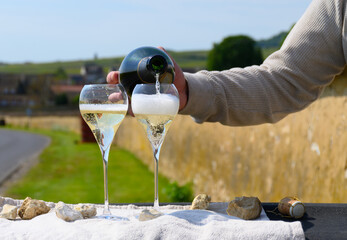 Pouring of grand cru sparkling white wine with bubbles champagne with view on old houses of Oger,...