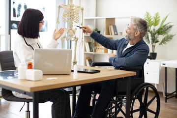Full length view of female physician and man with disability examining skeleton model while staying...