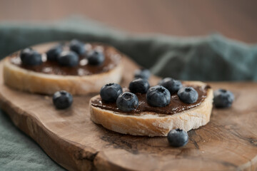 Organic chocolate hazelnut spread with fresh blueberries on ciabatta slices on wood board