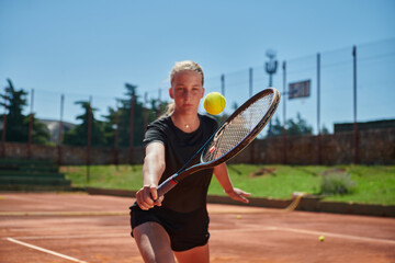 A young girl showing professional tennis skills in a competitive match on a sunny day, surrounded by the modern aesthetics of a tennis court.