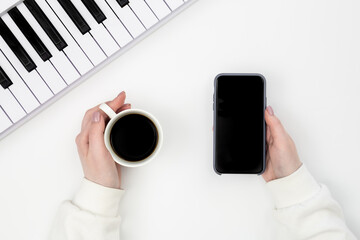 Smartphone, a cup of coffee in female hands and an electronic piano on a white background, top...
