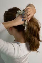 Naklejka premium Beige scrunchie, hair tie, being used making ponytail, long blond natural hair. Caucasian woman against white background.