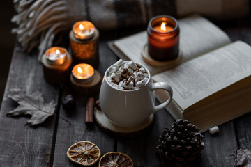 Obraz na płótnie Canvas Autumn cozy home composition with hot chocolate with marshmallow and candles. Aromatherapy on a grey fall morning, atmosphere of cosiness and relax. Wooden background, books, close up.