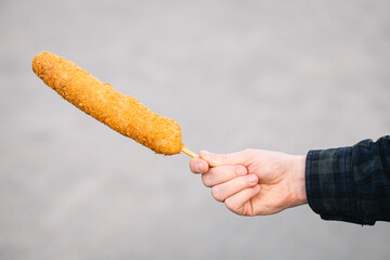 Man holding corn dog in paper plates on blurred background, korean street food.
