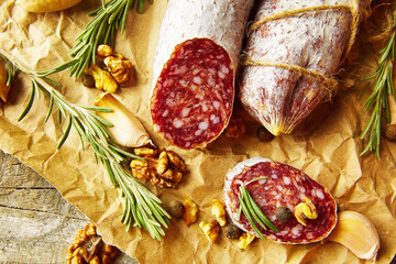 Italian salami wih sea salt, rosemary, garlic and nuts on paper. Rustic style. Top view. - 605034667