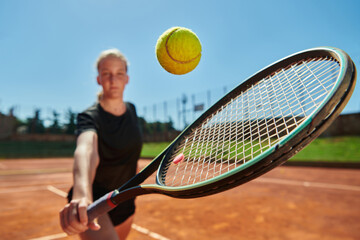 Close up photo of a young girl showing professional tennis skills in a competitive match on a sunny day, surrounded by the modern aesthetics of a tennis court.