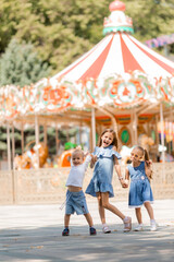 three small children are happily walking in the amusement park in the summer. International...