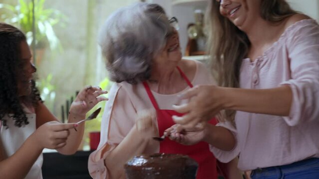 av&oacute; m&atilde;e e filha brasileiras se divertindo na cozinha brincando de passar cobertura de bolo no rosto uma da outra no dia das m&atilde;es