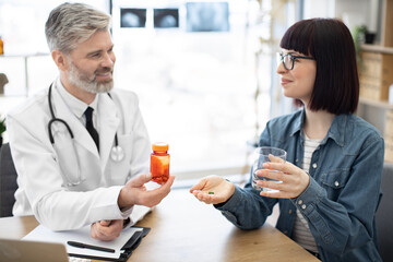 Obraz premium Cropped view of caucasian lady in eyeglasses receiving medicine from male physician in white coat at hospital. Focused patient starting full course of treatment according to written prescription.