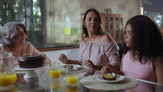avó mãe e filha latinas sentadas na mesa de jantar comendo bolo no dia das mães