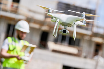 Drone operated by safety engineering inspector. Construction worker piloting drone on building site - obrazy, fototapety, plakaty