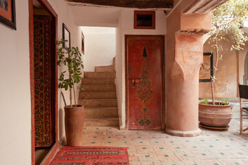 Interior of the entrance of a riyad with stairs, moroccan rugs, plants and red doors in Marrakech, Morocco