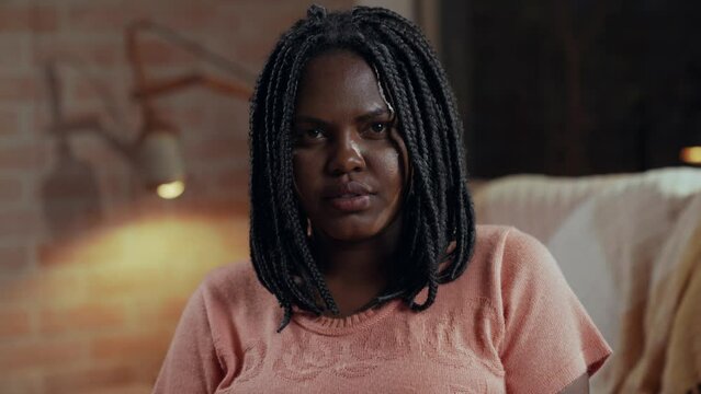 mulher negra brasileiro sentada no sofá da sala olhando para a câmera e sorrindo