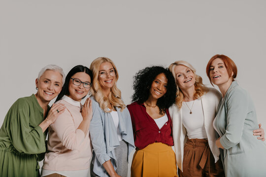 Multi-ethnic group of elegant mature women bonding and smiling against grey background