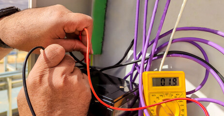 hands of an electrical technician checking with a polymeter the voltage and the correct...