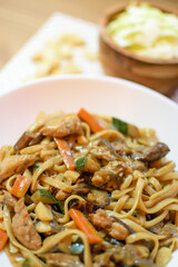 Rice noodles served with vegetables and meat in white bowl.