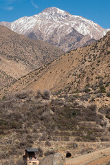 Peak of a snow mountain above the dirt mountains of the Ourika Valley in Morocco