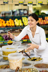 Young woman shopper in casual clothes picking olives at grocery store