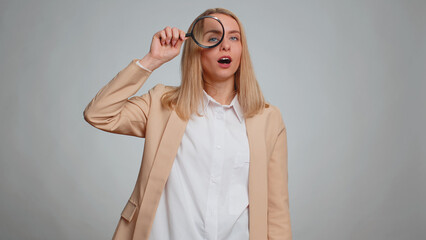 Investigator researcher scientist office woman holding magnifying glass near face, looking into camera with big zoomed funny eyes, searching analysing. Business girl isolated on gray studio background