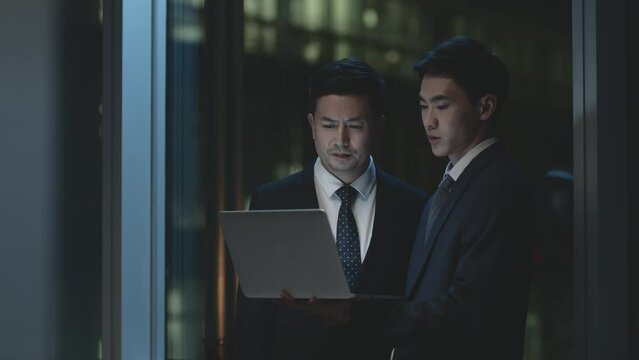 two young asian corporate executives working together late in office discussing business