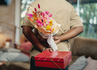 Latin man surprising his girlfriend with flowers and a gift on Valentine's Day no Brazil