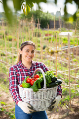 Satisfied young Hispanic woman engaged in cultivation of organic vegetables in her small garden showing good harvest