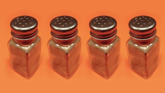 pepper shakers full of condiment turn on orange background