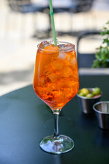Waiter prepared the Aperol Sprits summer cocktail with Aperol, prosecco, ice cubes and orange in wine glass, ready to drink on sunny terrace